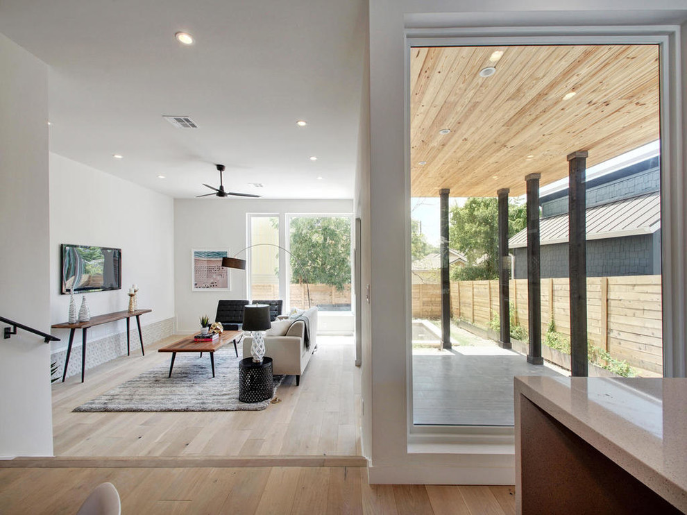 Imagen de salón abierto moderno de tamaño medio sin chimenea con paredes blancas, suelo de madera clara y televisor colgado en la pared