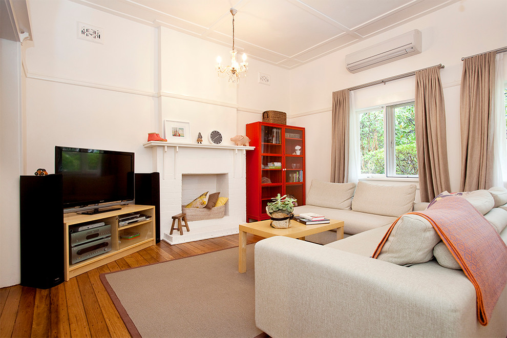 Cette photo montre un salon éclectique avec un mur blanc, un sol en bois brun, une cheminée standard, un manteau de cheminée en brique et un téléviseur indépendant.