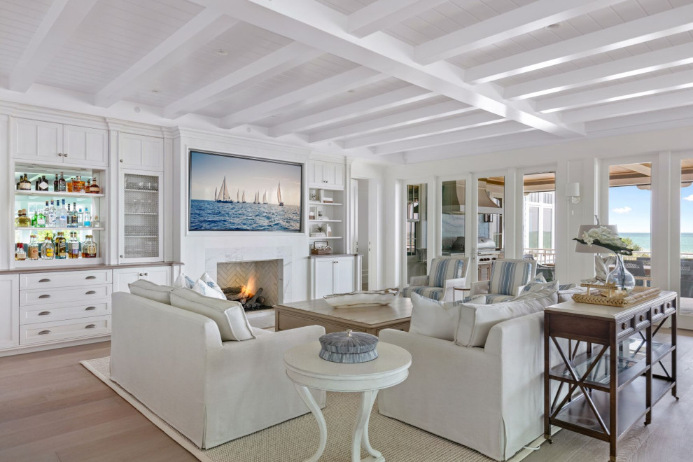 Photo of a large coastal open plan living room in Tampa with a home bar, white walls, medium hardwood flooring, a standard fireplace, a stone fireplace surround, a wall mounted tv and grey floors.