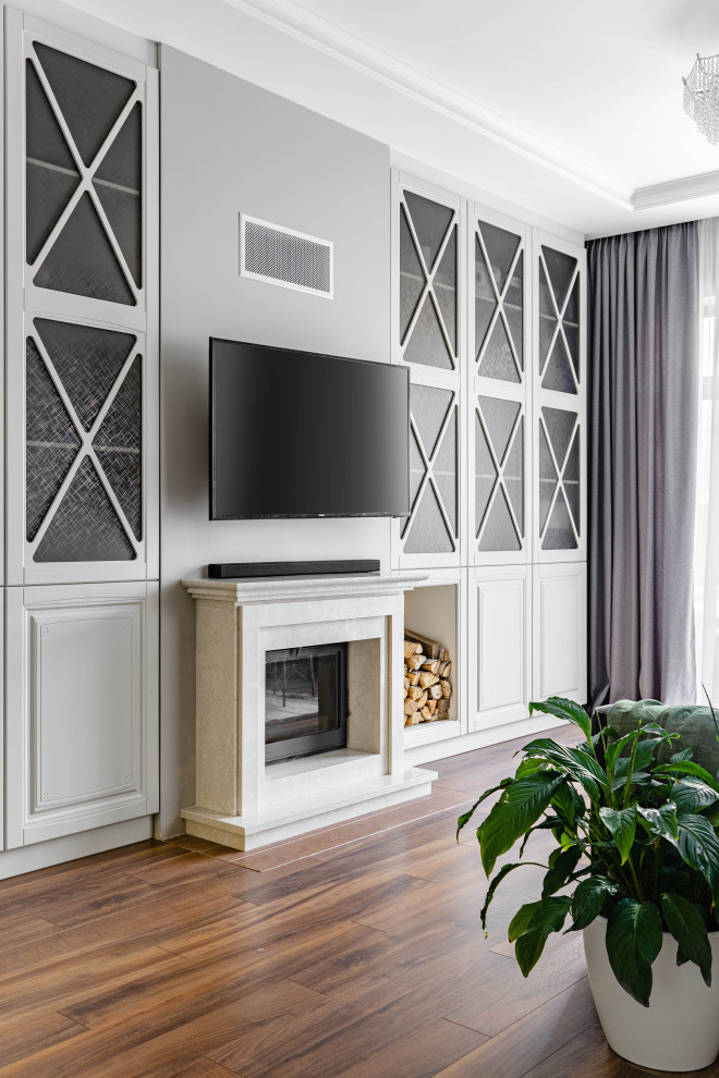Пример оригинального дизайна: гостиная комната среднего размера в стиле неоклассика (современная классика) с с книжными шкафами и полками, серыми стенами, паркетным полом среднего тона, стандартным камином, фасадом камина из камня, телевизором на стене и коричневым полом