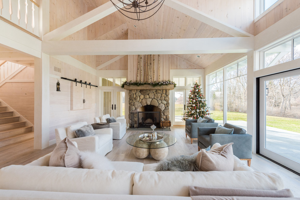 This is an example of a large rustic formal open plan living room in New York with beige walls, light hardwood flooring, a standard fireplace, a stone fireplace surround, a concealed tv and beige floors.