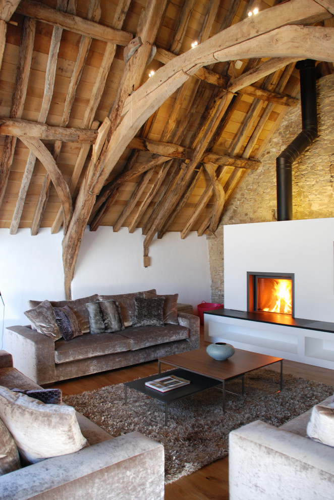 Design ideas for a large rustic mezzanine living room in Cornwall with white walls, a wood burning stove, a wall mounted tv, medium hardwood flooring, a plastered fireplace surround and a vaulted ceiling.