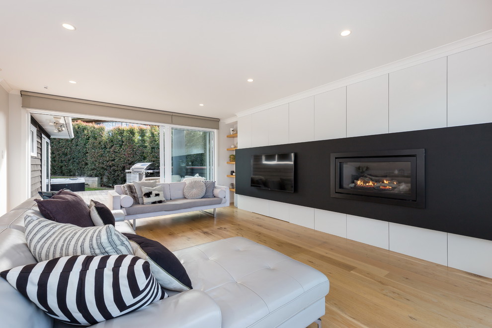 Large contemporary open plan living room in Auckland with white walls, light hardwood flooring, a standard fireplace, a plastered fireplace surround, a built-in media unit and beige floors.