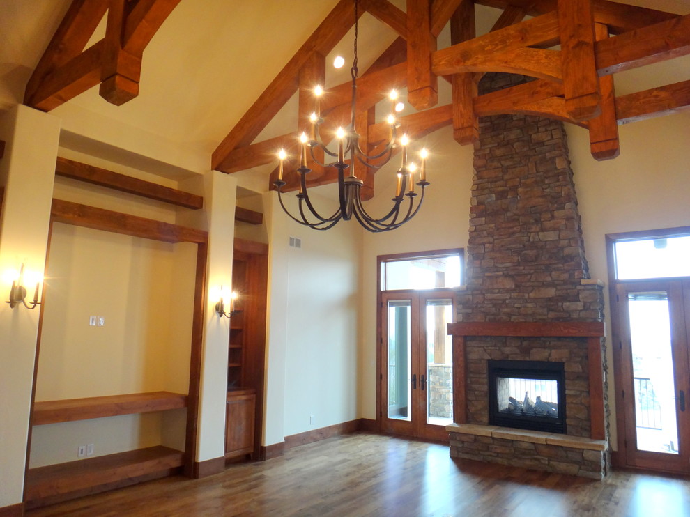 Aménagement d'un grand salon montagne ouvert avec une salle de réception, un mur beige, un sol en bois brun, une cheminée double-face, un manteau de cheminée en pierre et un téléviseur encastré.