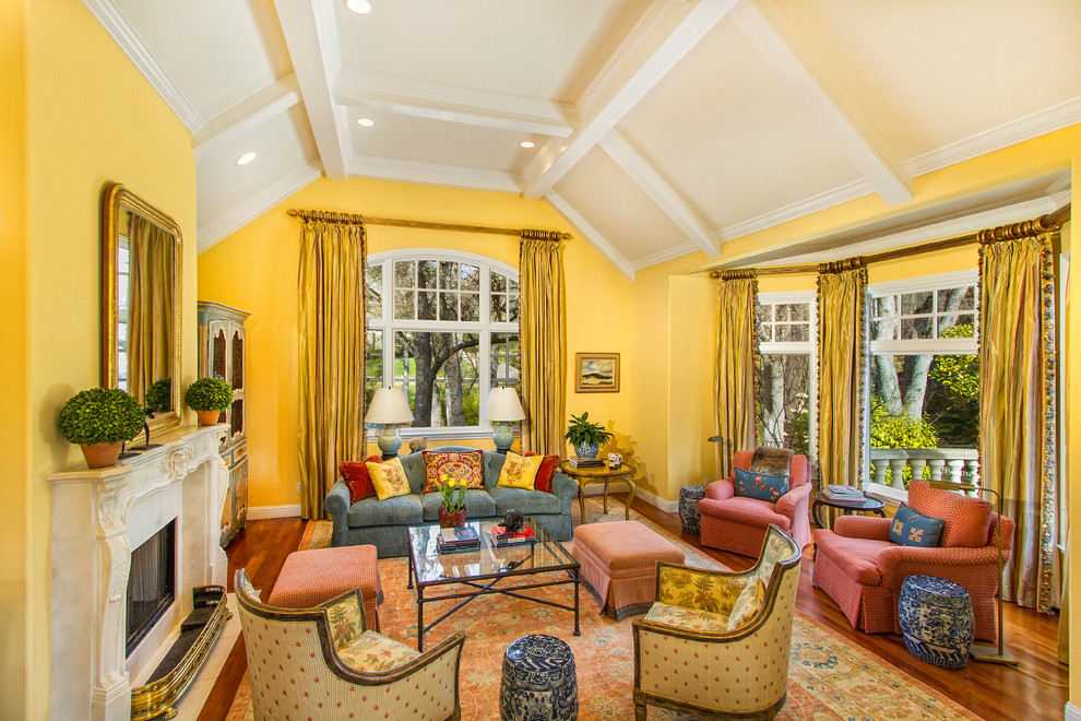 Cette image montre un salon traditionnel de taille moyenne et fermé avec un mur jaune, une cheminée standard, une salle de réception, un sol en bois brun, un manteau de cheminée en plâtre, aucun téléviseur et un sol marron.