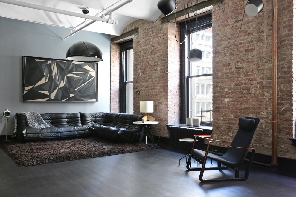 Aménagement d'un salon industriel avec un mur gris, parquet foncé et canapé noir.