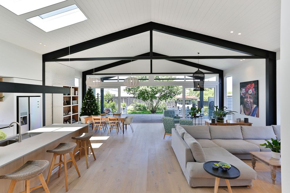 This is an example of a large traditional open plan living room in Auckland with white walls, light hardwood flooring, a ribbon fireplace, a wall mounted tv and brown floors.