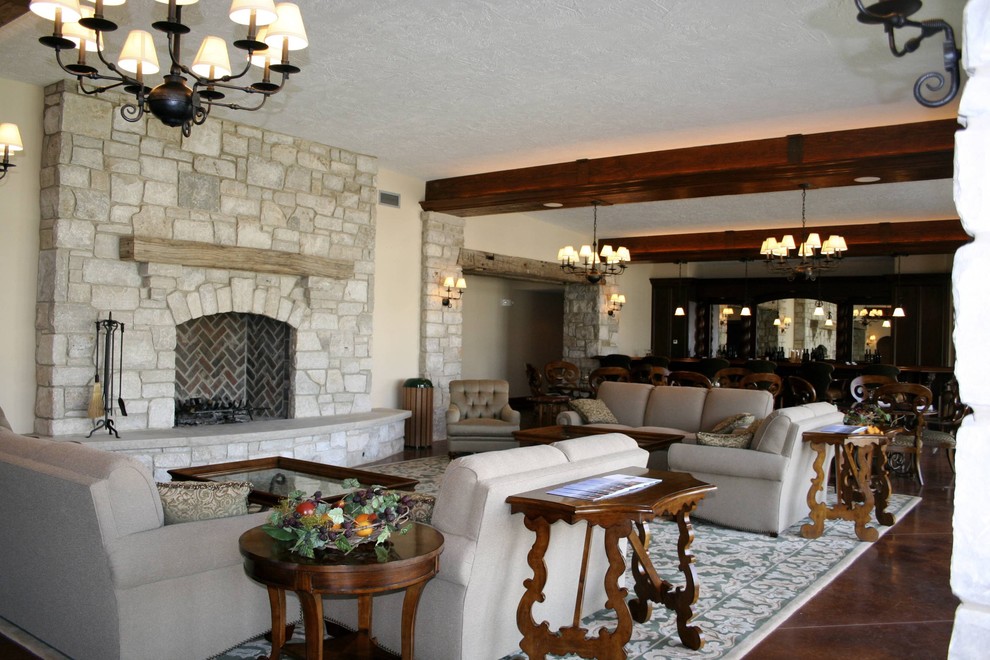 На фото: большая открытая гостиная комната в классическом стиле с домашним баром, бежевыми стенами, бетонным полом, стандартным камином, фасадом камина из камня и коричневым полом без телевизора