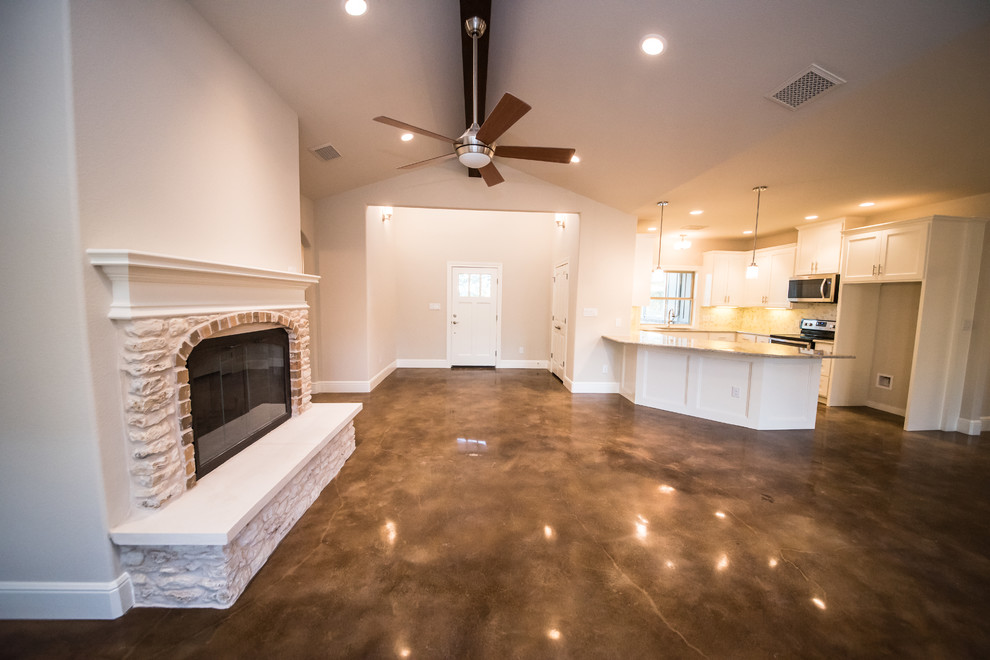 Offenes, Großes Uriges Wohnzimmer mit Betonboden, Kamin, Kaminumrandung aus Stein und beiger Wandfarbe in Austin