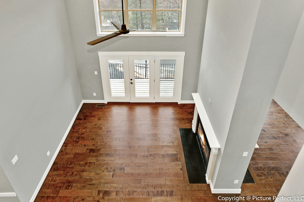 Cette photo montre un salon chic ouvert avec un mur gris, un sol en bois brun et une cheminée double-face.