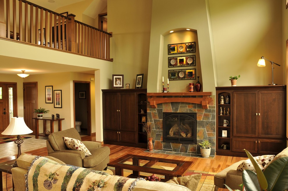 Cette image montre un salon ouvert avec une salle de réception, un mur vert, un sol en bois brun, une cheminée standard, un manteau de cheminée en carrelage et un téléviseur dissimulé.