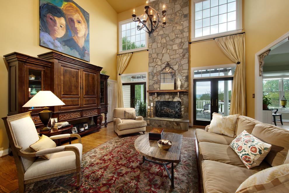 На фото: большая открытая гостиная комната в классическом стиле с желтыми стенами, стандартным камином, фасадом камина из камня, паркетным полом среднего тона и ковром на полу без телевизора