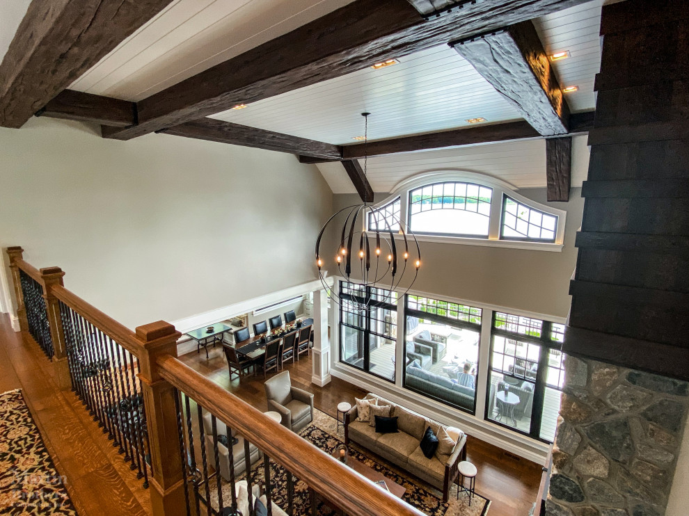 Example of a huge mountain style open concept medium tone wood floor, vaulted ceiling and wainscoting living room design in Other with beige walls, a standard fireplace, a stone fireplace and a wall-mounted tv