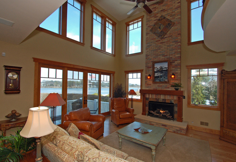Cette image montre un salon craftsman ouvert avec un bar de salon, un sol en bois brun, une cheminée standard, un manteau de cheminée en brique et un téléviseur dissimulé.