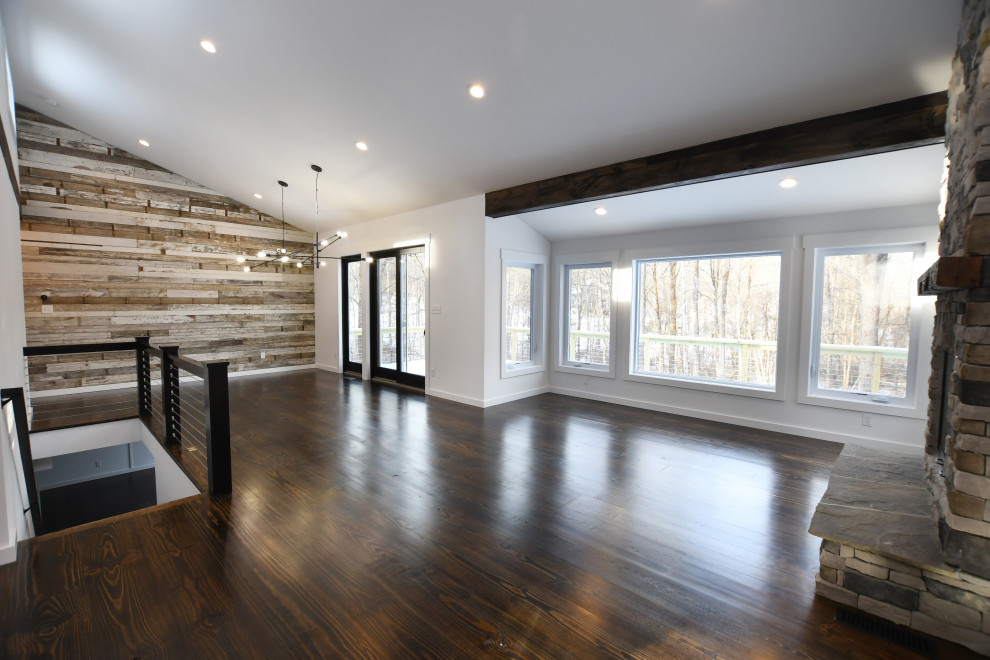 Großes, Offenes Retro Wohnzimmer mit weißer Wandfarbe, braunem Holzboden, Kamin, Kaminumrandung aus Stein und braunem Boden in New York