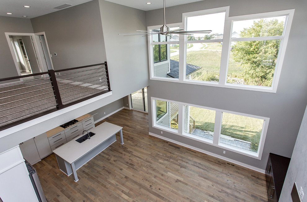 Cette image montre un grand salon design ouvert avec un mur gris, un sol en bois brun et un sol beige.