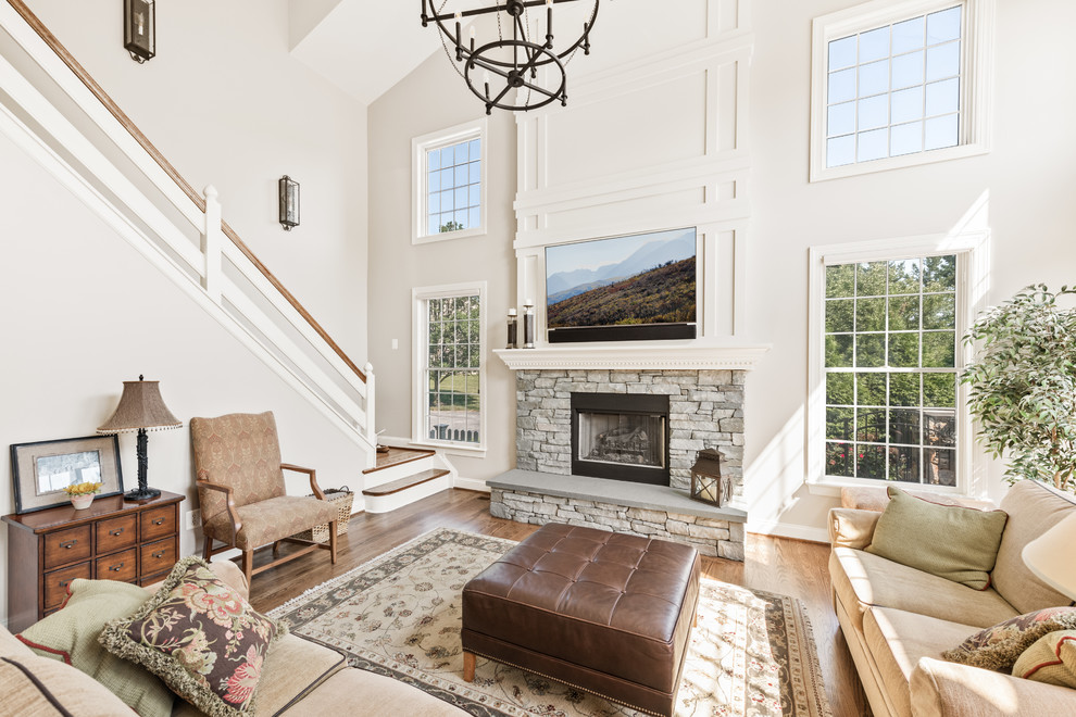 Photo of a large classic enclosed living room in Philadelphia with white walls, medium hardwood flooring, a standard fireplace, a stone fireplace surround, a wall mounted tv and brown floors.