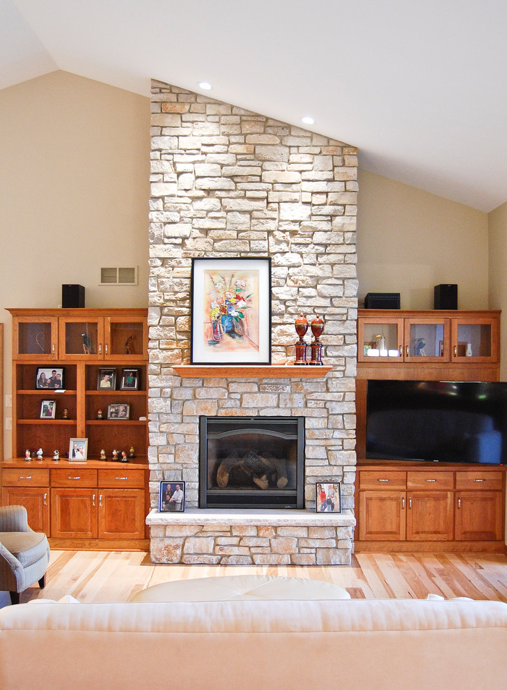 他の地域にあるトラディショナルスタイルのおしゃれなLDK (石材の暖炉まわり、ベージュの壁、淡色無垢フローリング、標準型暖炉、埋込式メディアウォール) の写真