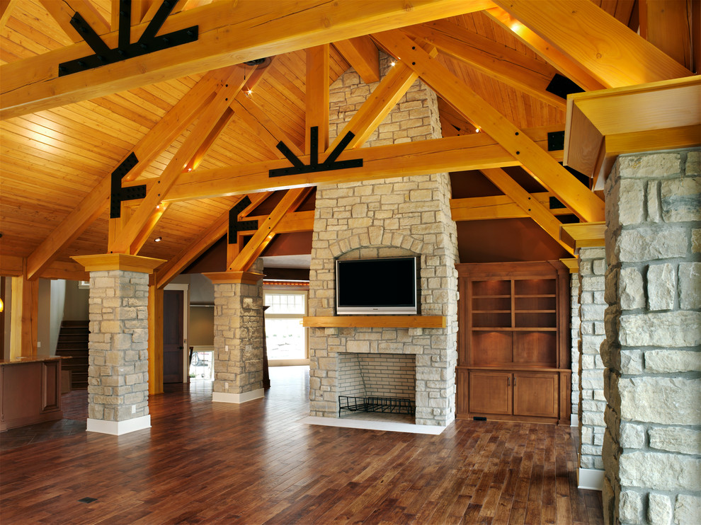 Ejemplo de salón abierto rural grande con paredes beige, suelo de madera en tonos medios, todas las chimeneas, marco de chimenea de piedra y televisor colgado en la pared