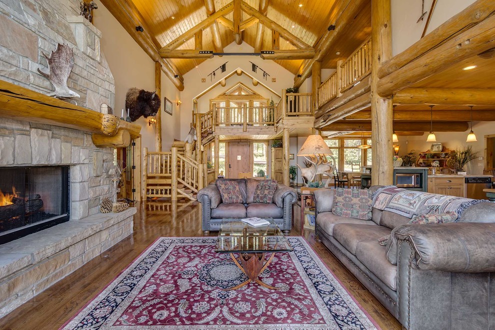 Rustikales Wohnzimmer mit beiger Wandfarbe, braunem Holzboden, Kamin, Kaminumrandung aus Stein und Steinwänden in Denver