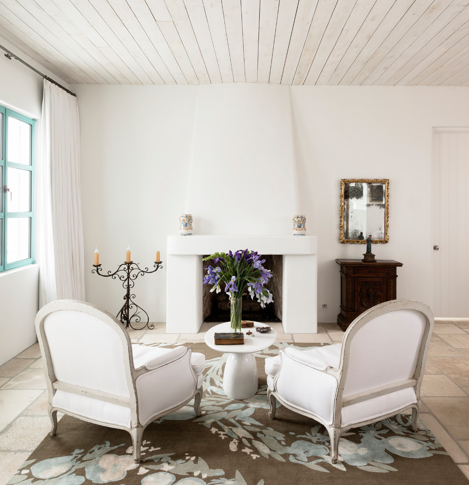 Aménagement d'un salon méditerranéen de taille moyenne et fermé avec un mur blanc, un sol en calcaire, une cheminée standard, un manteau de cheminée en plâtre, aucun téléviseur et une salle de réception.