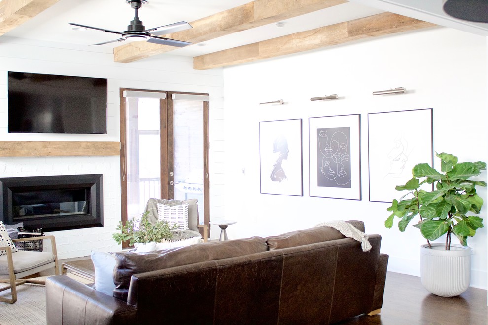 Imagen de salón abierto minimalista grande con paredes blancas, suelo de madera oscura, todas las chimeneas, marco de chimenea de ladrillo, televisor colgado en la pared y suelo marrón