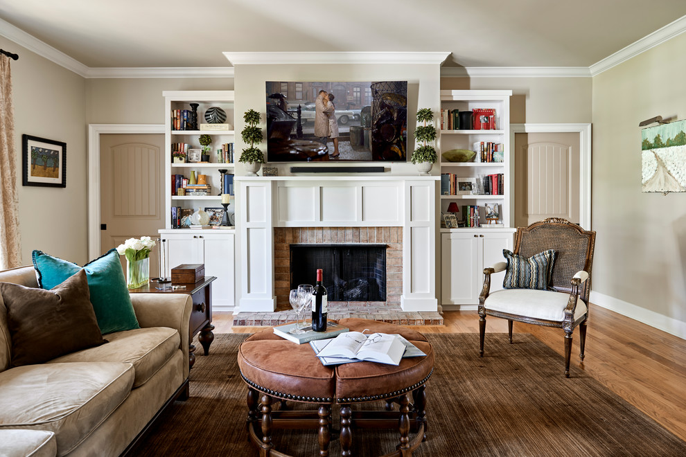 Exemple d'un salon chic avec une cheminée standard, un téléviseur fixé au mur, un mur beige, un sol en bois brun, un manteau de cheminée en brique et un sol marron.