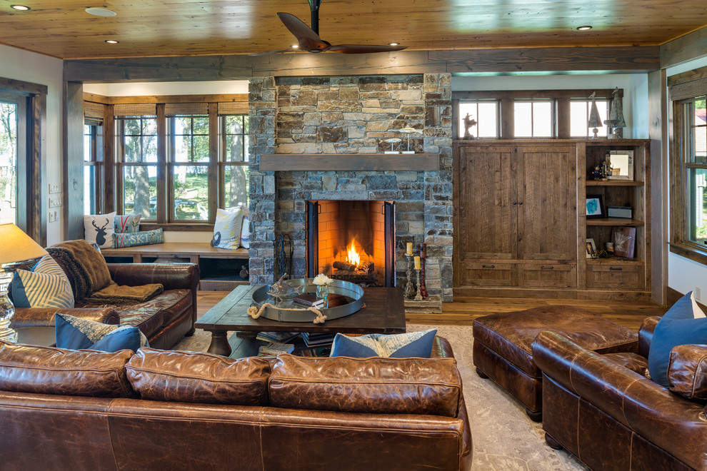 Example of a mountain style dark wood floor and brown floor living room design in Minneapolis with white walls, a standard fireplace and a stone fireplace