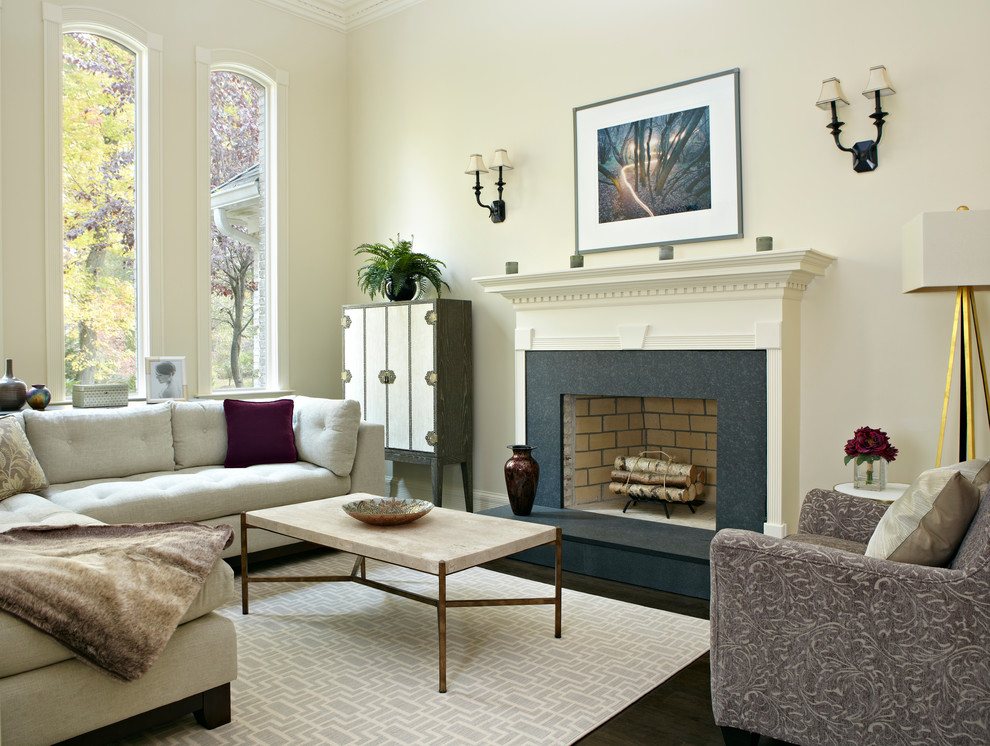 На фото: гостиная комната в стиле неоклассика (современная классика) с белыми стенами, темным паркетным полом и стандартным камином без телевизора