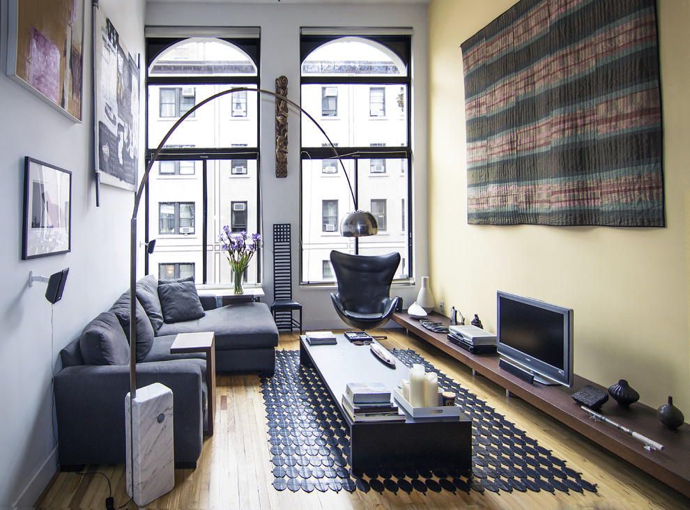 Example of a small minimalist formal medium tone wood floor and brown floor living room design in New York with a tv stand, yellow walls and no fireplace