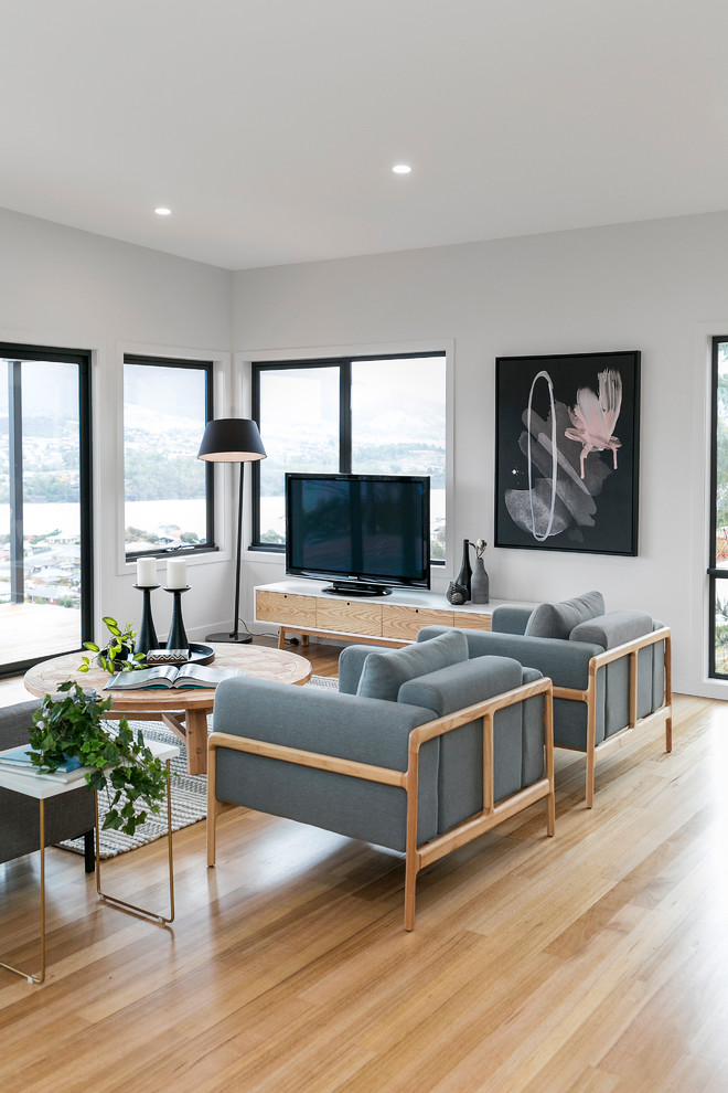 Skandinavisk inredning av ett vardagsrum, med vita väggar, ljust trägolv och en fristående TV