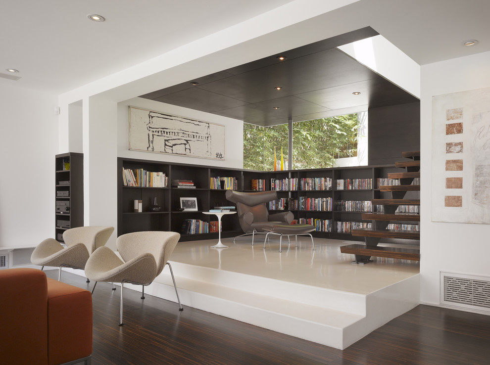 Exempel på ett litet modernt allrum med öppen planlösning, med ett bibliotek, vita väggar och mörkt trägolv