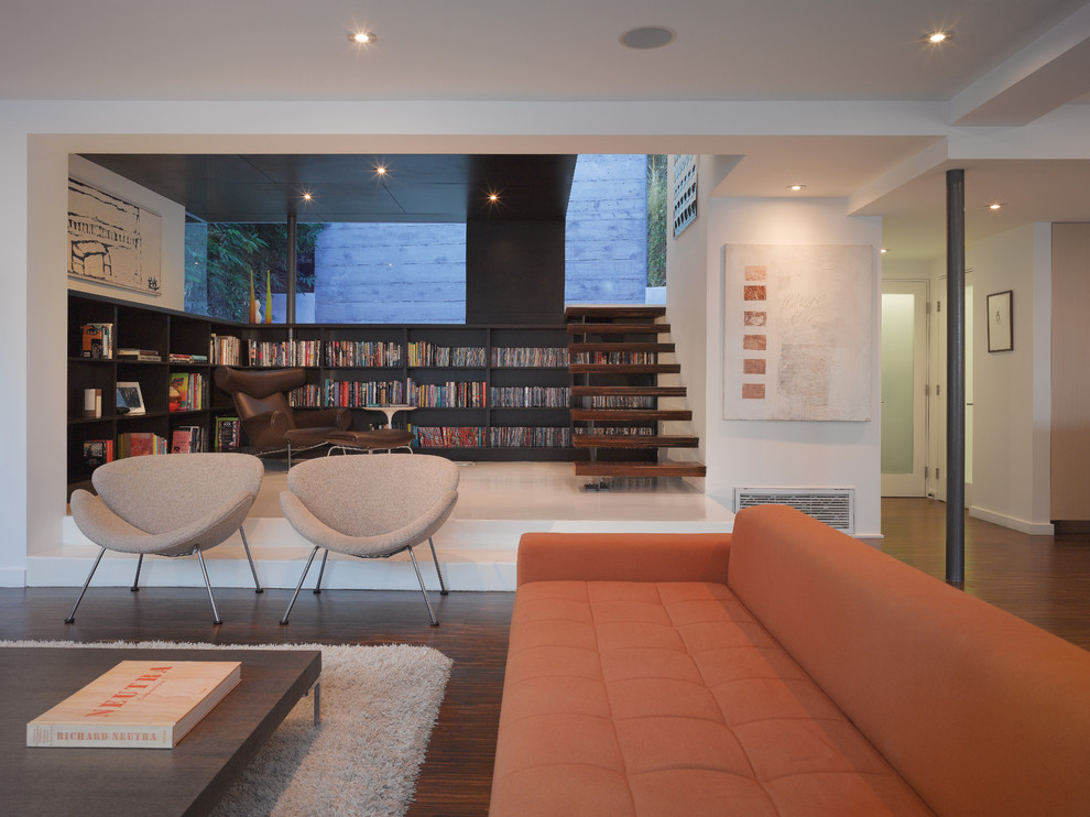Réalisation d'un petit salon minimaliste ouvert avec une bibliothèque ou un coin lecture, un mur blanc et parquet foncé.