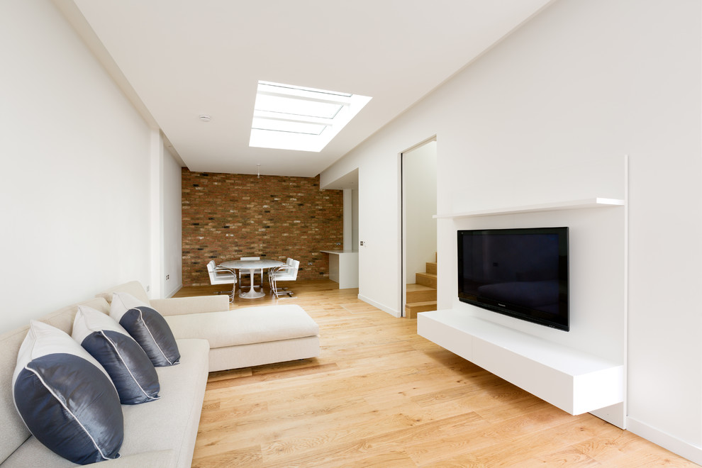 Modelo de salón abierto contemporáneo de tamaño medio con suelo de madera en tonos medios, suelo marrón, paredes blancas y televisor colgado en la pared