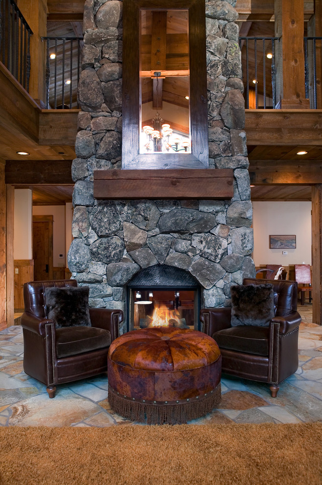 Пример оригинального дизайна: гостиная комната в стиле рустика с двусторонним камином и фасадом камина из камня