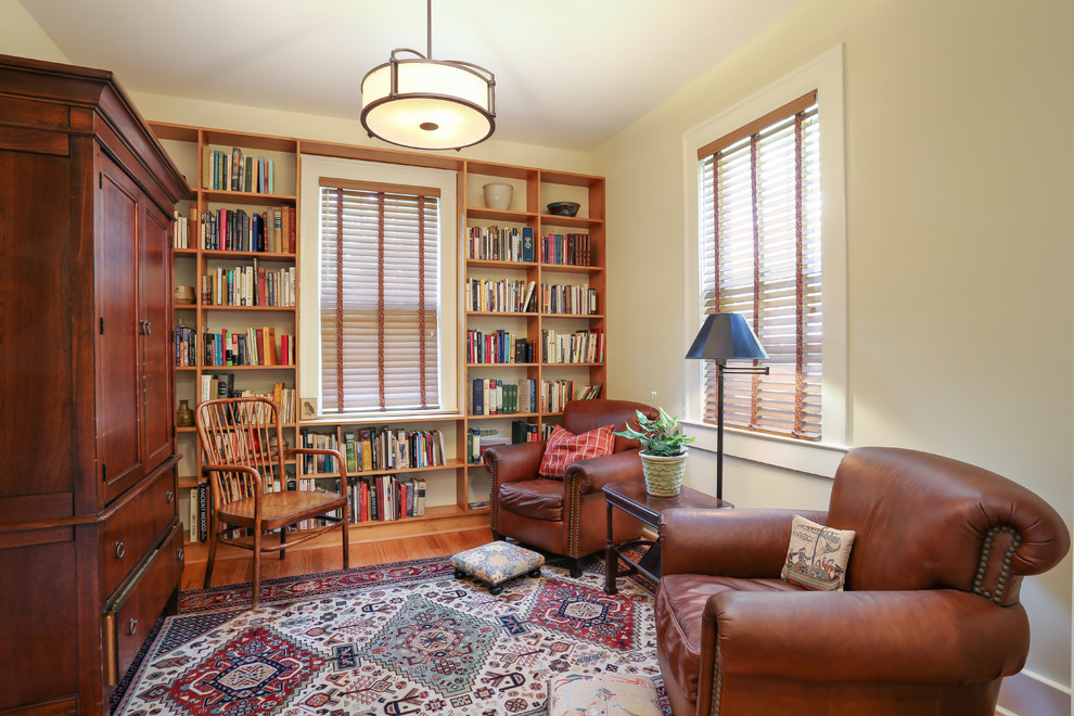 Cette image montre un petit salon traditionnel fermé avec une bibliothèque ou un coin lecture, un mur jaune et un sol en bois brun.