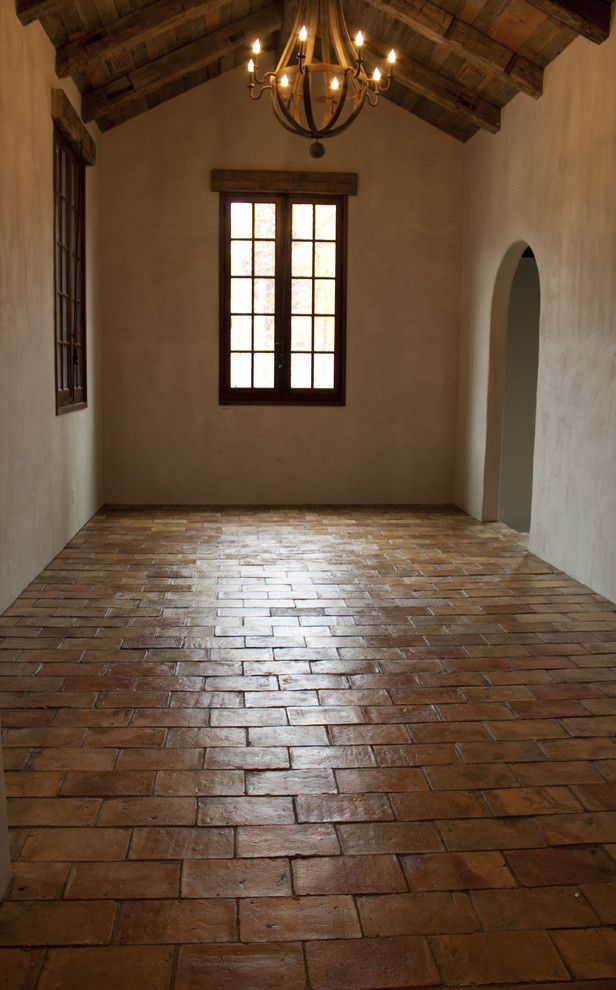 На фото: большая открытая гостиная комната в средиземноморском стиле с полом из терракотовой плитки и фасадом камина из камня