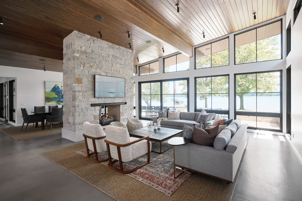 Пример оригинального дизайна: огромная открытая гостиная комната в современном стиле с бетонным полом, двусторонним камином, телевизором на стене и серым полом
