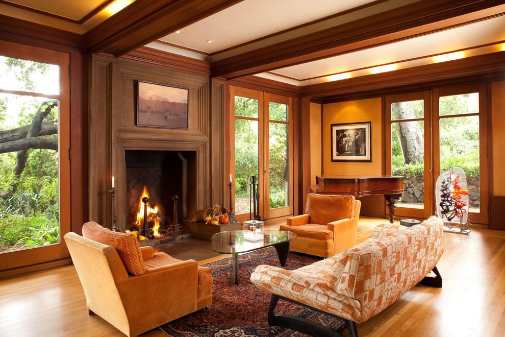 Diseño de salón de estilo americano con parades naranjas, suelo de madera en tonos medios, marco de chimenea de madera y suelo naranja