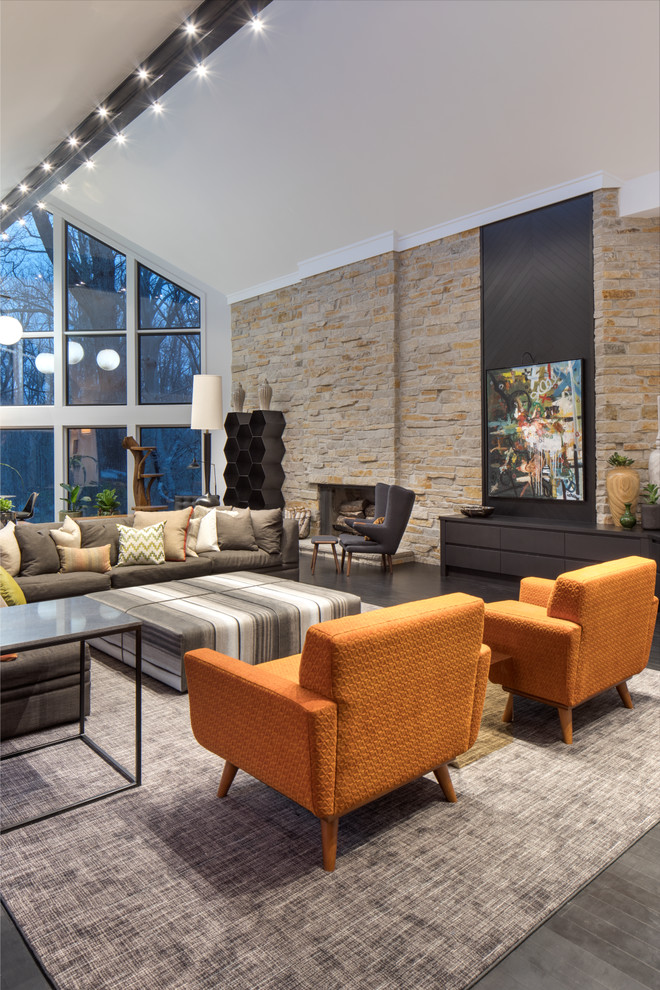 На фото: огромная открытая гостиная комната в стиле неоклассика (современная классика) с серыми стенами, темным паркетным полом, стандартным камином, фасадом камина из камня, телевизором на стене и черным полом