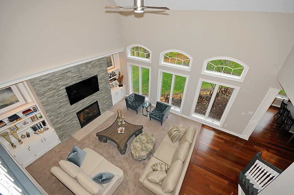 Пример оригинального дизайна: большая парадная, открытая гостиная комната в стиле неоклассика (современная классика) с серыми стенами, ковровым покрытием, стандартным камином, фасадом камина из камня и телевизором на стене