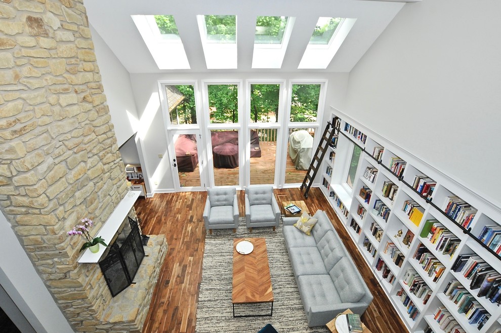 Foto på ett stort funkis allrum med öppen planlösning, med ett bibliotek, grå väggar, mellanmörkt trägolv, en standard öppen spis, en spiselkrans i sten och brunt golv