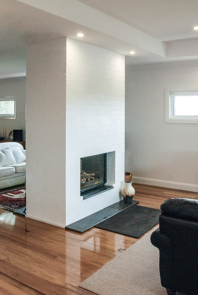 Photo of a medium sized contemporary open plan living room in Adelaide with white walls, medium hardwood flooring, a two-sided fireplace, a brick fireplace surround and brown floors.