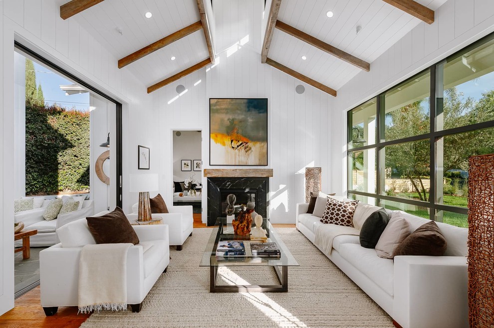 Landhausstil Wohnzimmer mit weißer Wandfarbe, braunem Holzboden, Kamin, Kaminumrandung aus Stein und braunem Boden in Los Angeles