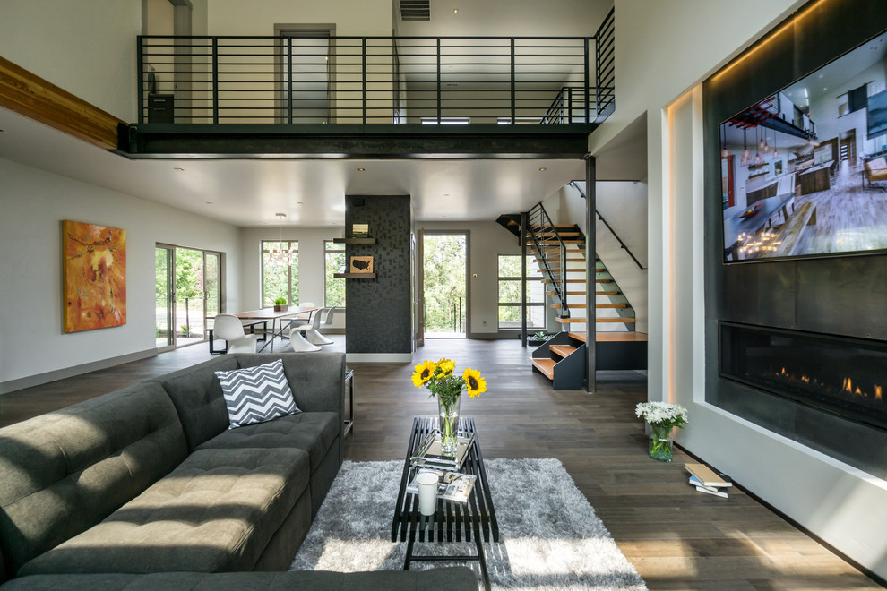 Diseño de salón abierto moderno grande con paredes grises, suelo de madera en tonos medios, chimenea lineal, marco de chimenea de metal y televisor colgado en la pared
