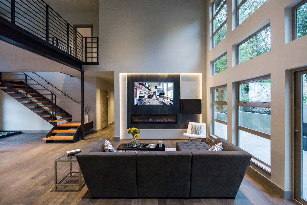 Ejemplo de salón abierto moderno grande con paredes grises, suelo de madera en tonos medios, chimenea lineal, marco de chimenea de metal y televisor colgado en la pared