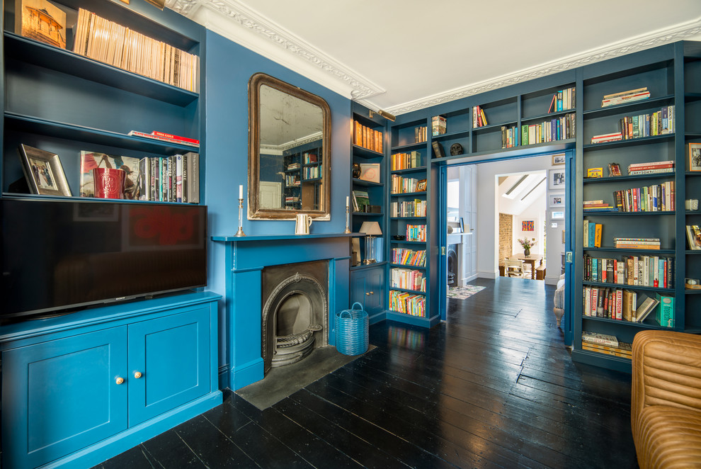 Klassisk inredning av ett vardagsrum, med blå väggar, målat trägolv, en standard öppen spis, en spiselkrans i trä och svart golv