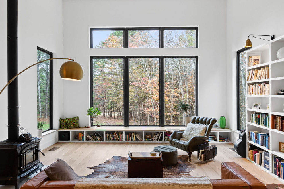 Diseño de biblioteca en casa abierta contemporánea sin televisor con paredes blancas, suelo de madera clara, estufa de leña y suelo beige