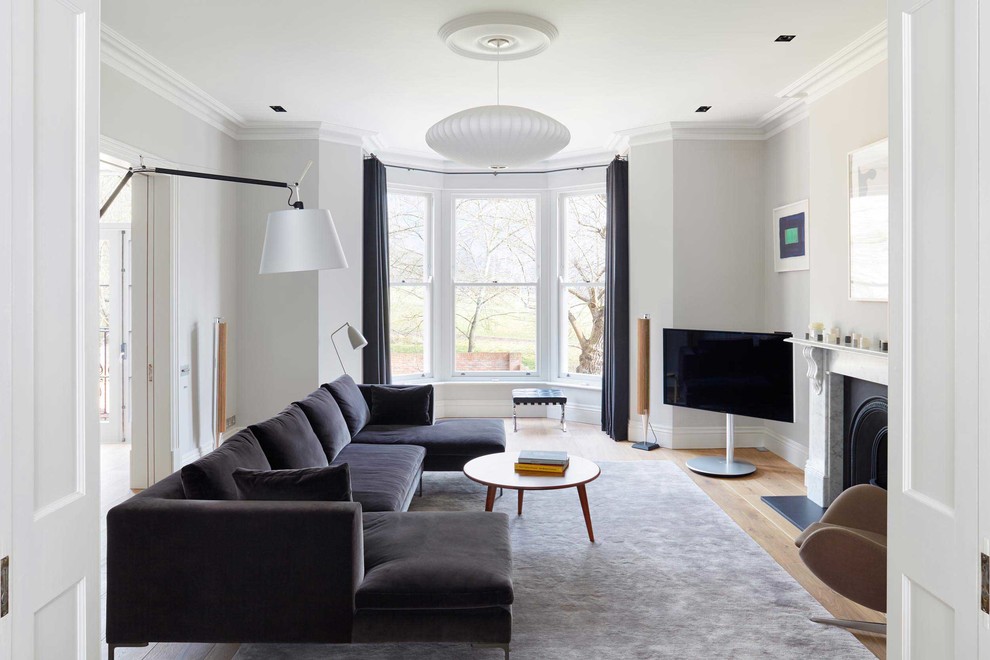 Mittelgroßes Klassisches Wohnzimmer mit grauer Wandfarbe, hellem Holzboden, Kamin, Kaminumrandung aus Stein und freistehendem TV in London