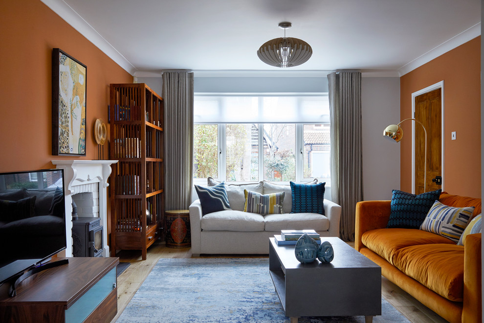 Mittelgroßes Klassisches Wohnzimmer mit oranger Wandfarbe, hellem Holzboden, Kaminofen, Kaminumrandung aus Backstein, freistehendem TV und beigem Boden in London